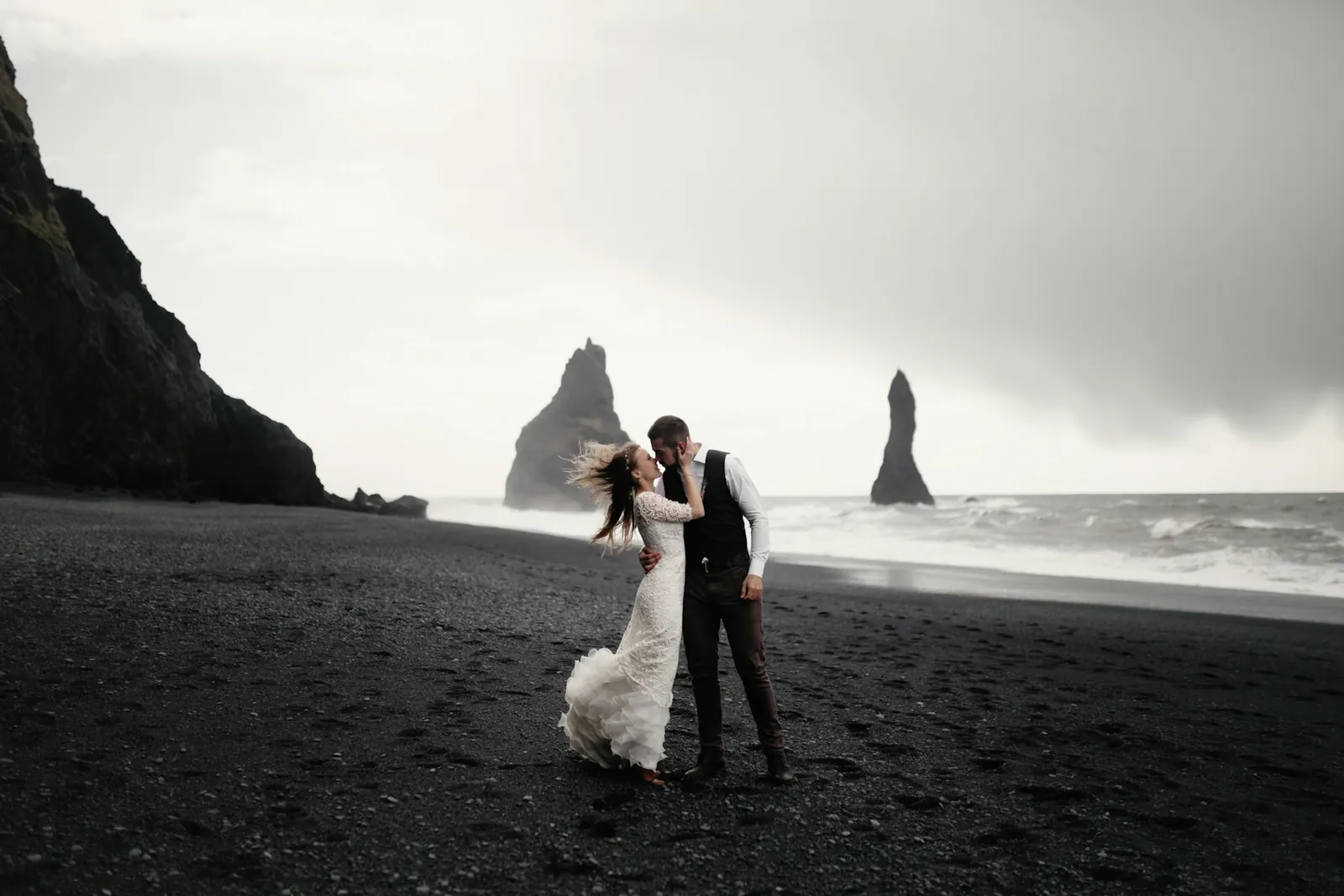 Couple embracing on a black sand beach beneath sea stacks