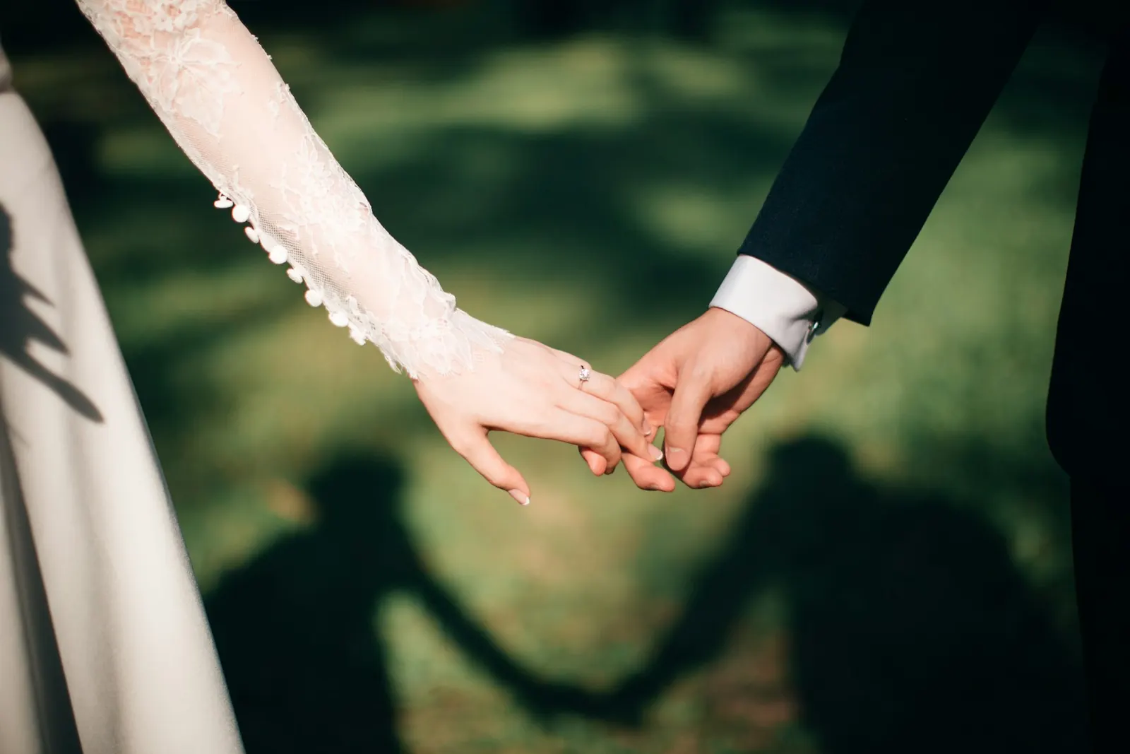 Bride and groom holding hands with their shadows on the grass