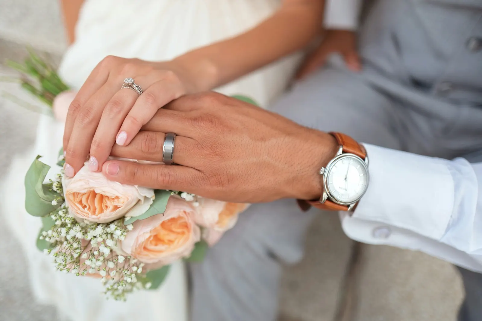 Couple's hands with wedding rings and a small bouquet