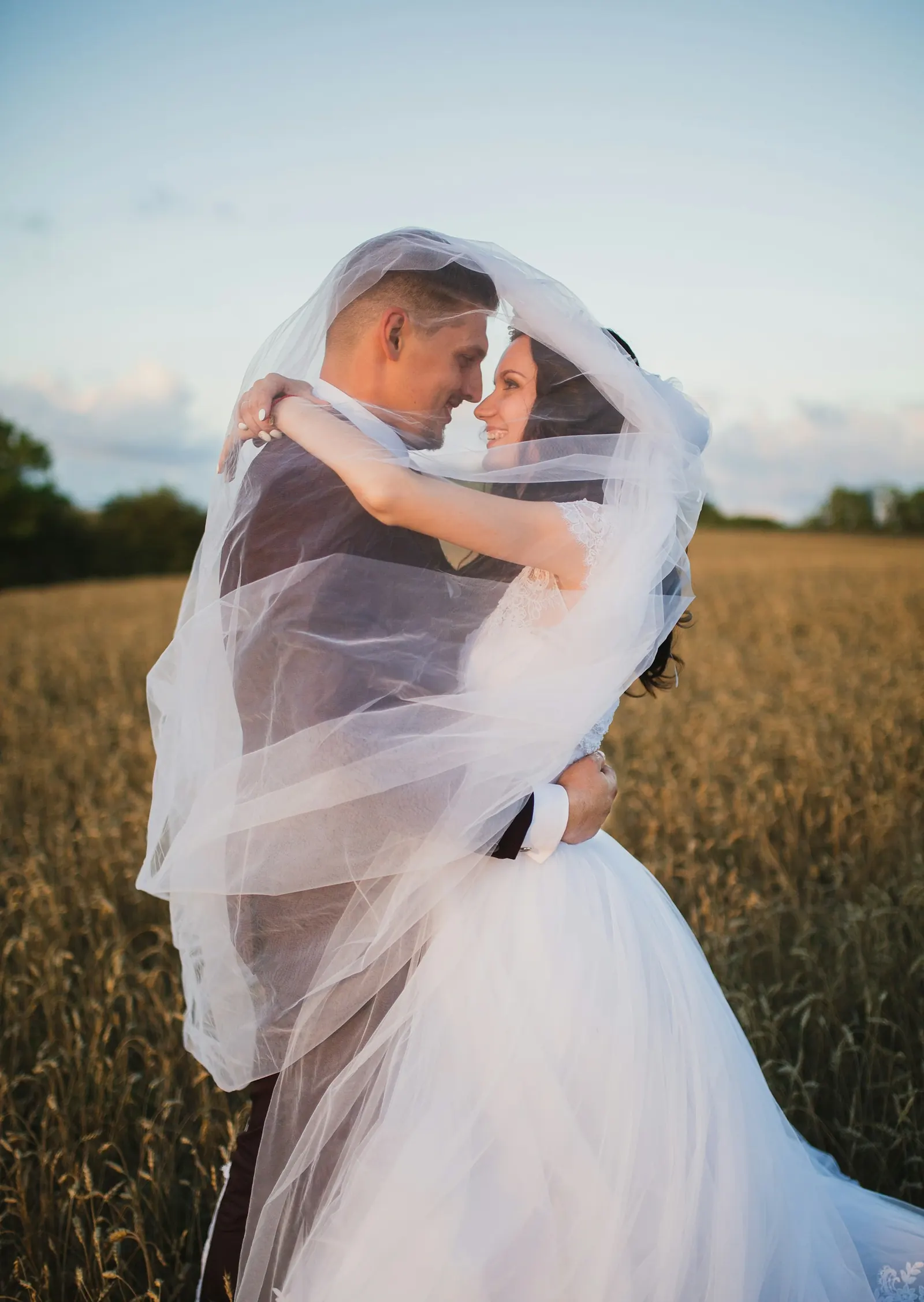 Groom wrapping the bride in her veil in a golden field